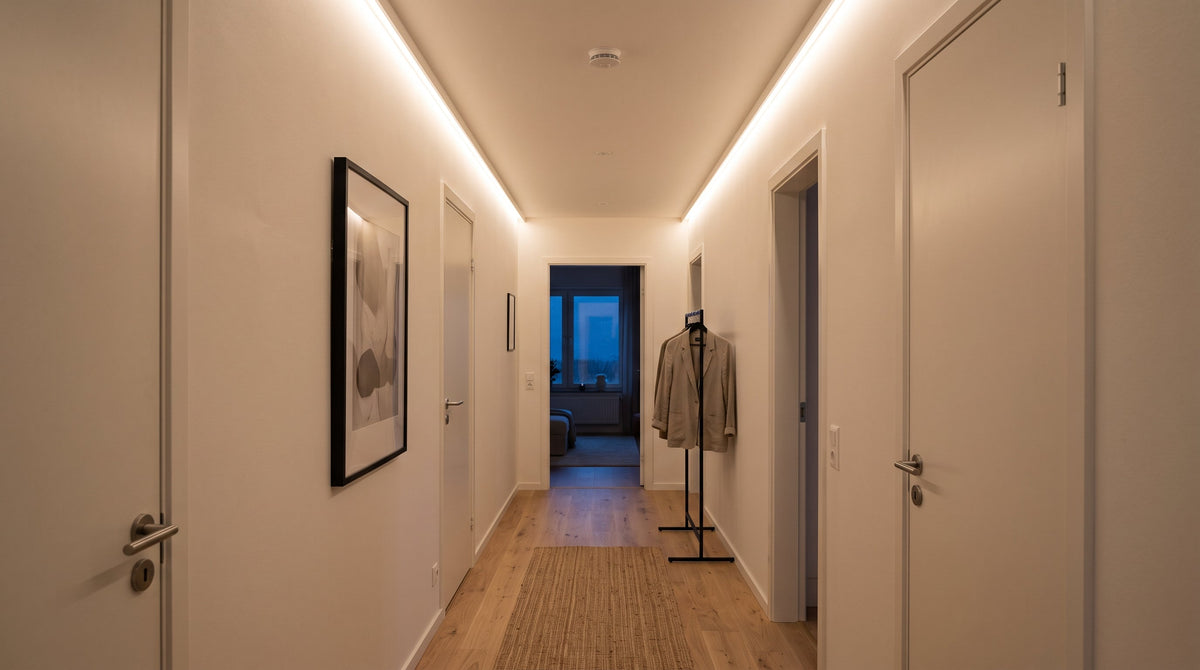 Schmaler Flur mit indirektem warmweißem LED-Streifen an der oberen Wandkante, dessen Licht Decke und Wand aufhellt und den Flur breiter wirken lässt